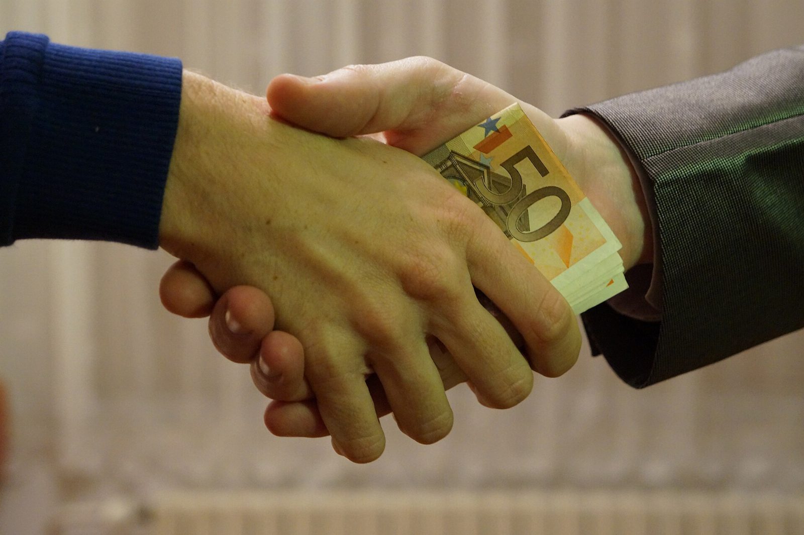 Zwei Hände beim Handschlag, zwischen ihnen ein Bündel 50-Euro-Scheine