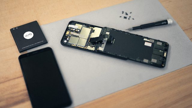 Geöffnetes Smartphone auf einer Arbeitsunterlage, daneben Akku, Ersatzdisplay und Schraubendreher