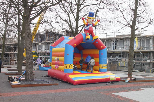 Bunte aufblasbare Hüpfburg mit einer Clownfigur auf dem Dach, darin spielen drei Kinder, im Hintergrund kahle Bäume