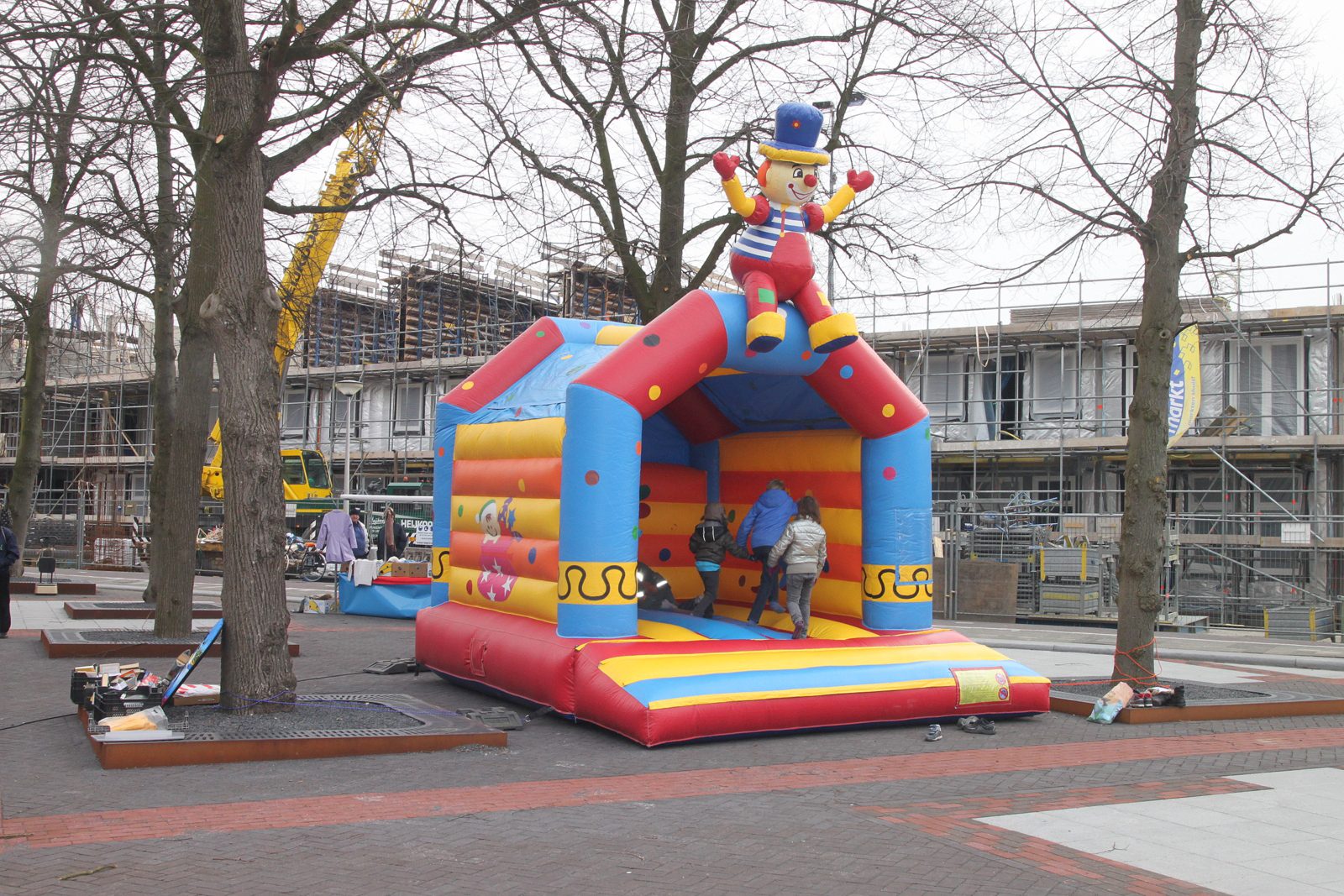 Bunte aufblasbare Hüpfburg mit einer Clownfigur auf dem Dach, darin spielen drei Kinder, im Hintergrund kahle Bäume
