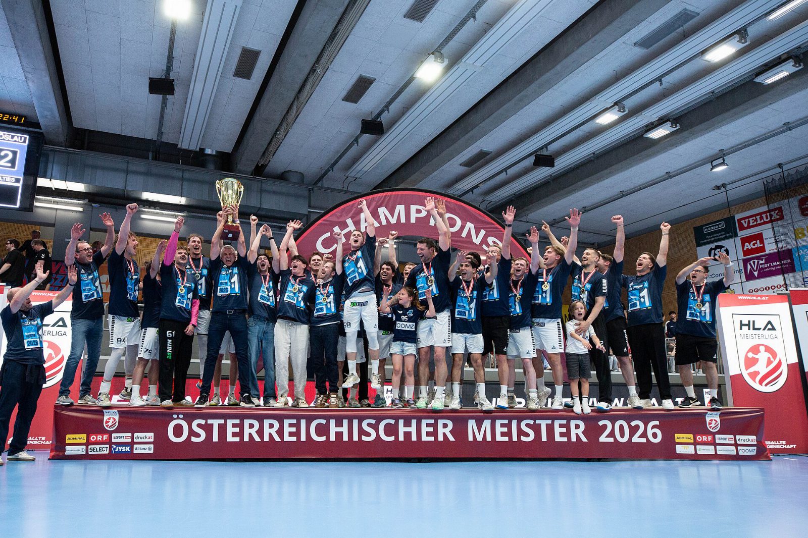 Handballer der Jags Vöslau jubeln mit Pokal auf einem Podest mit der Aufschrift Österreichischer Meister 2026