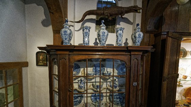Ausgestopftes Krokodil auf einem alten Holzschrank, davor fünf blau-weiße Delfter Vasen, in einem Museumsraum mit Holzbalken