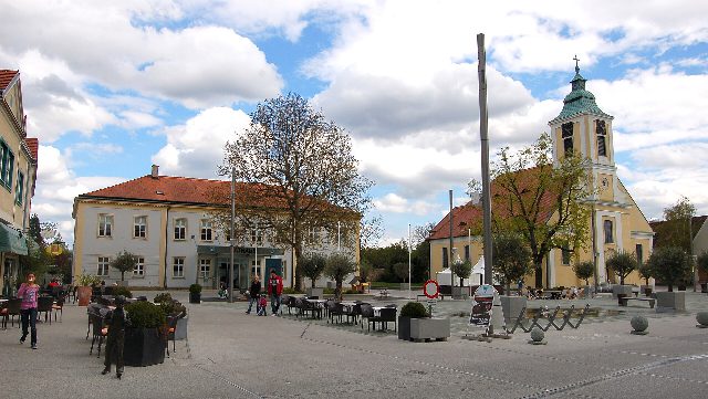 Kirchenplatz in Leobersdorf mit dem Rathaus links und der gelben Pfarrkirche zum heiligen Martin mit grünem Turmdach rechts