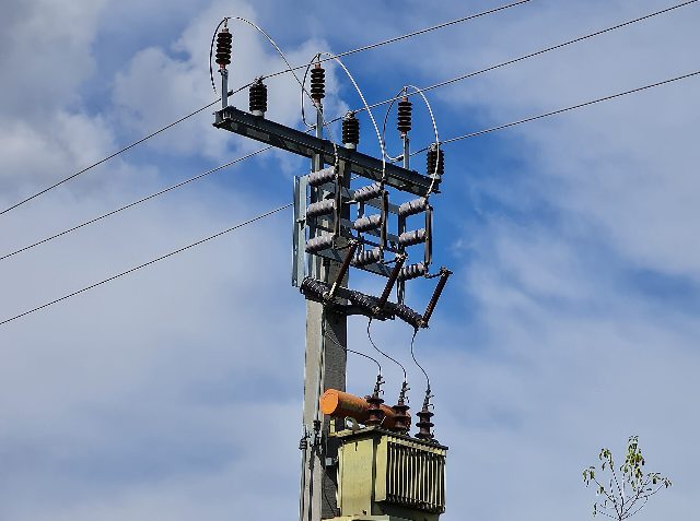 Masttransformator der Wiener Netze in Kottingbrunn: Betonmast mit Isolatoren, Trennschaltern und Transformator vor blauem Himmel