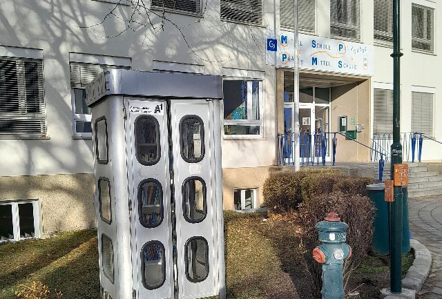 Eingang der Mittelschule Pelzgasse in Baden, davor eine Bücherzelle. Das bisherige Schulgebäude, nicht der geplante Neubau