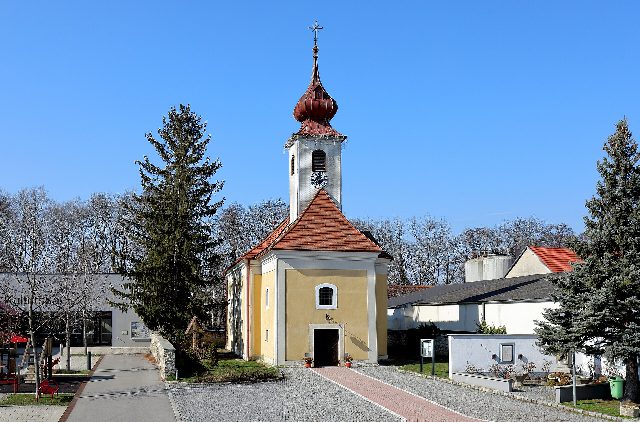 Pfarrkirche hl. Katharina in Mitterndorf an der Fischa mit Zwiebelturm, links der Kultursaal und ein Spielplatz mit roten Bänken