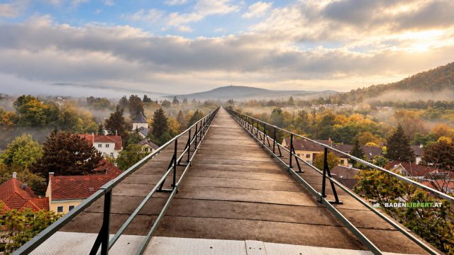 Blick über den Steg am Aquädukt bei Baden auf Hausdächer, Herbstwald und Morgennebel, im Hintergrund ein bewaldeter Hügel