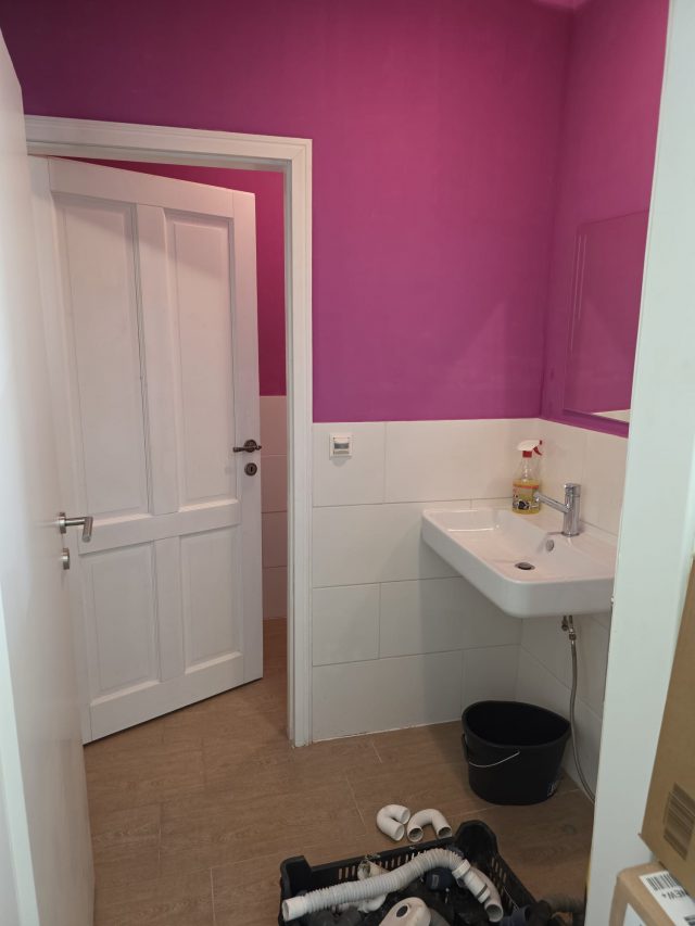 Waschraum mit pink gestrichener Wand, weißem Waschbecken und Montagematerial am Boden