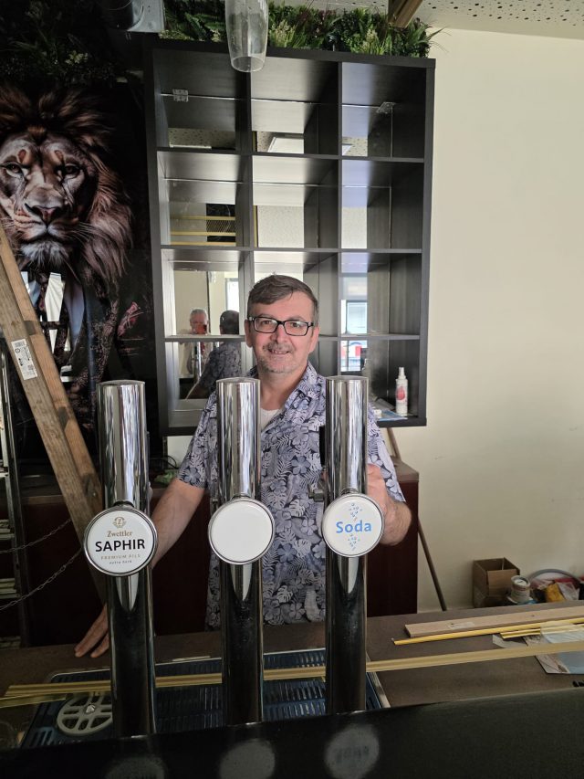Drei Zapfsäulen an der fertigen Bar, dahinter ein Mitarbeiter und das Regal mit Spiegelrückwand