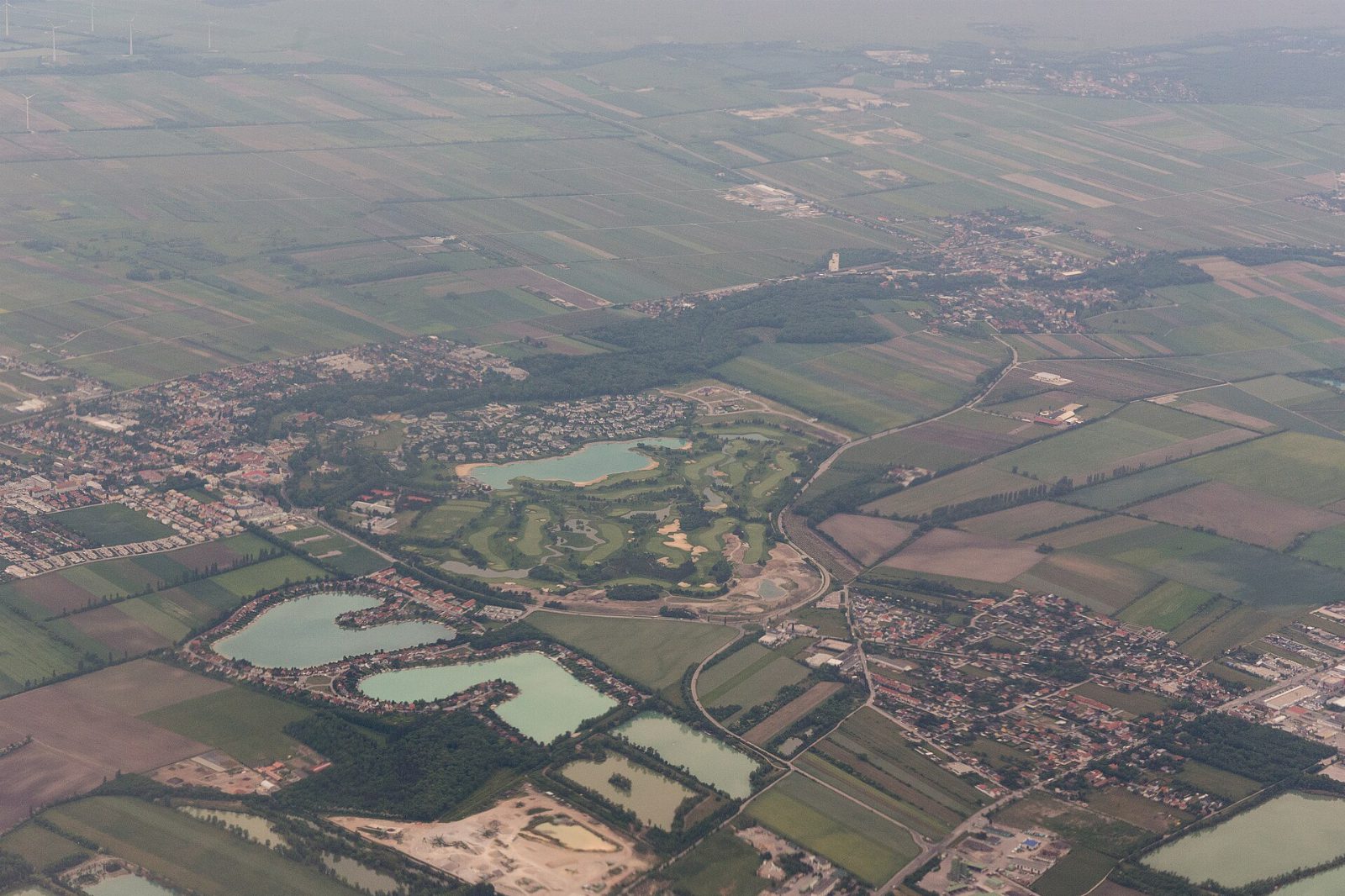 Luftbild von Oberwaltersdorf mit Siedlungen, einem Golfplatz und mehreren türkisen Teichen zwischen Feldern