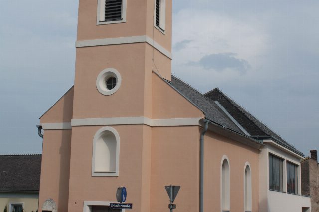 Pfarrkirche Oeynhausen in Traiskirchen, rosa verputzter Bau mit Turm, an der Ecke ein Straßenschild Triesterstraße