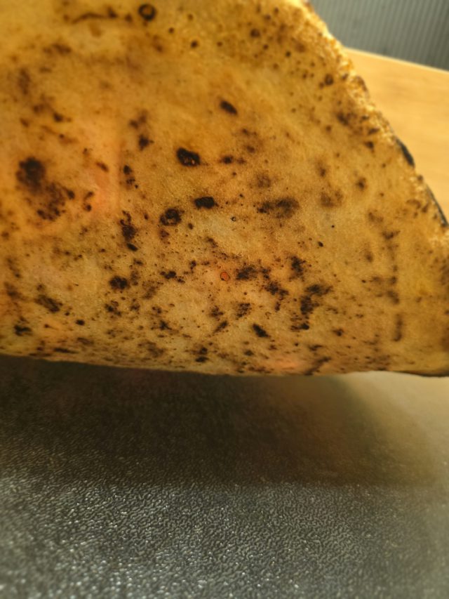 Unterseite der gelieferten Pizza mit sichtbaren Backspuren.