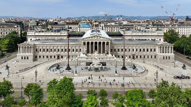 Das Parlamentsgebäude in Wien von vorne, mit Säulenportal und Athene-Brunnen, davor die Rampe, Bäume und die Ringstraße