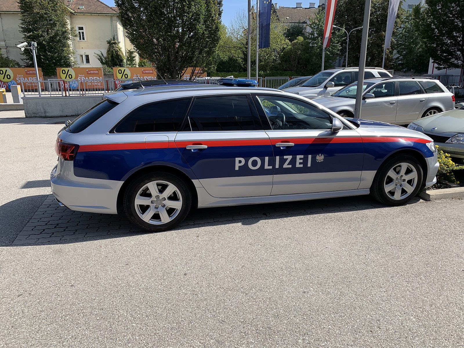 Silberner Streifenwagen der österreichischen Polizei mit blau-rotem Streifen und Schriftzug Polizei, seitlich auf einem Parkplatz
