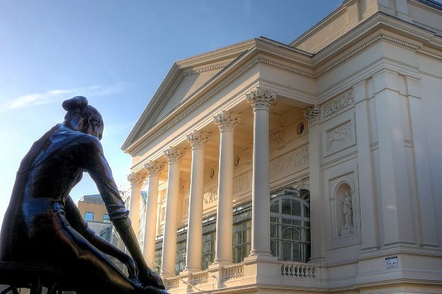 Säulenfassade des Royal Opera House in London, davor die Bronzestatue einer sitzenden Ballerina