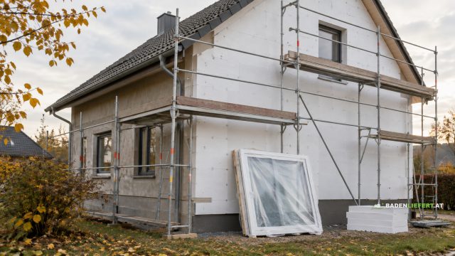 Symbolbild: eingerüstetes Einfamilienhaus mit neuen Dämmplatten und einem verpackten Fenster an der Wand