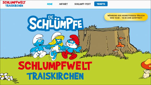 Startseite der Schlumpfwelt Traiskirchen: Schlumpf, Schlumpfine und Papa Schlumpf laufen Hand in Hand über eine Wiese vor einem Baumstumpf, darüber das Logo „Die Schlümpfe“, rechts oben der Hinweis „Während der Herbstferien täglich von 10:00 – 18:30 Uhr geöffnet!“