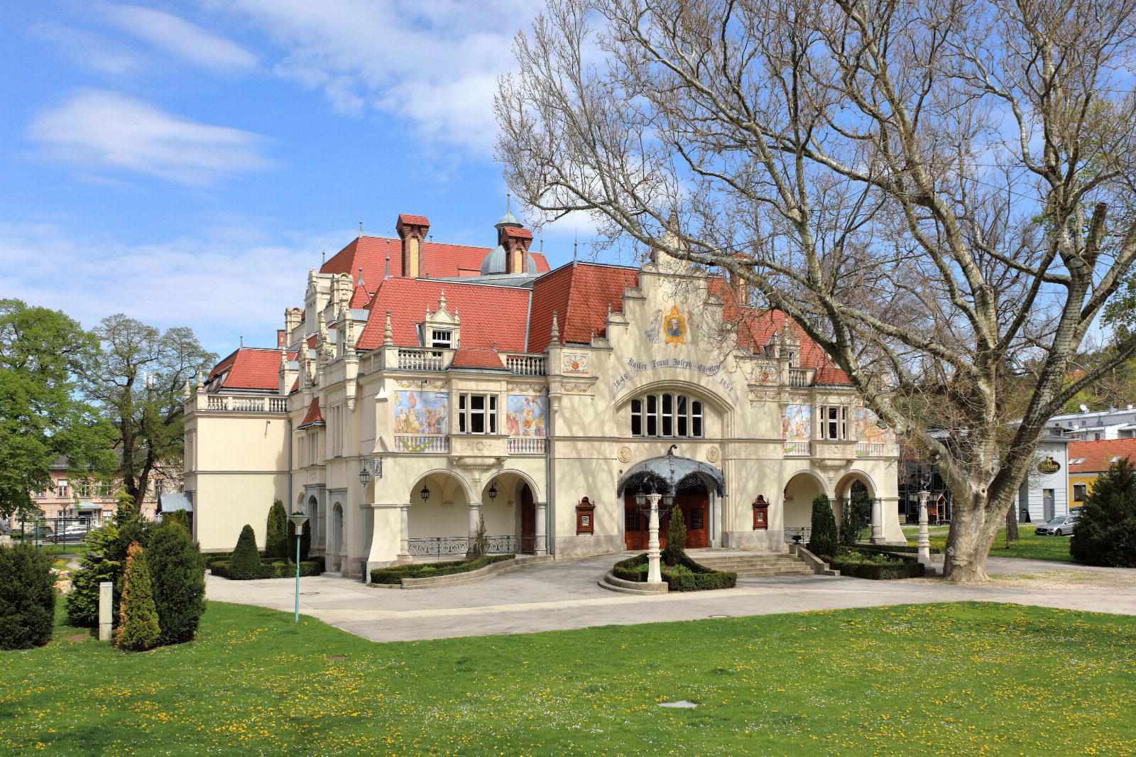 Das Stadttheater Berndorf mit verzierter Fassade, roten Dächern und Wiese davor