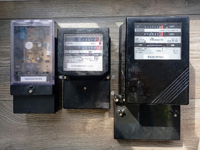 Drei ausgebaute schwarze Stromzähler mit Zählwerken in Kilowattstunden nebeneinander auf einem Holzbrett