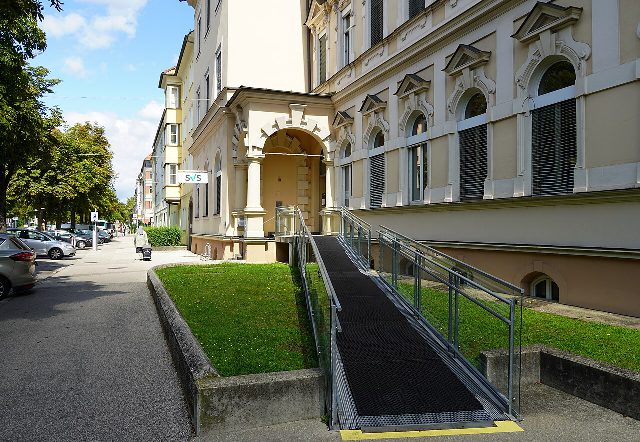 Gebäude der Sozialversicherung der Selbständigen in Klagenfurt mit SVS-Schild, Säulenportal und einer Rampe mit Geländer zum Eingang