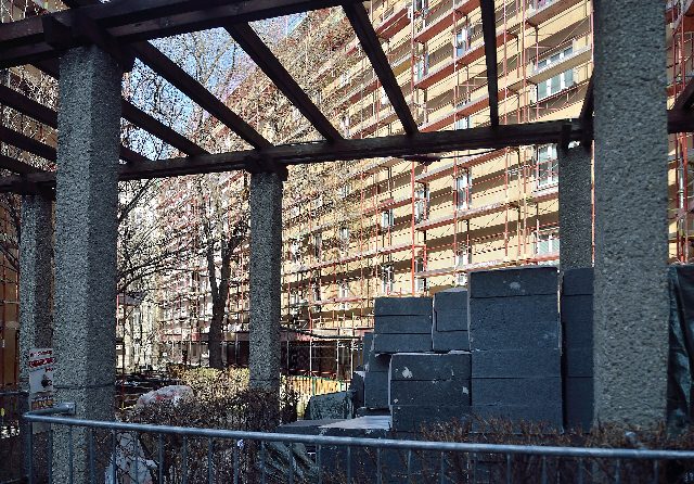 Thermische Sanierung eines Wohnbaus in Wien: eingerüstete Fassade, im Vordergrund gestapelte graue Dämmplatten unter einer Pergola