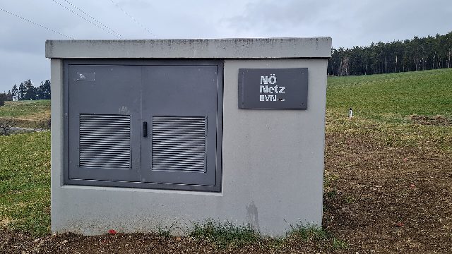 Graue Trafostation mit Schild „NÖ Netz EVN“ am Rand einer Wiese