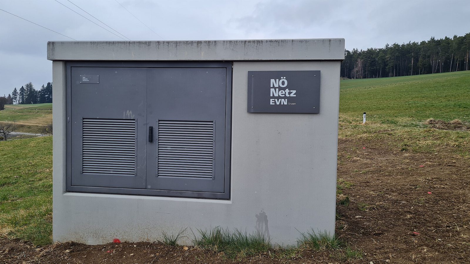 Graue Trafostation mit Schild „NÖ Netz EVN“ am Rand einer Wiese