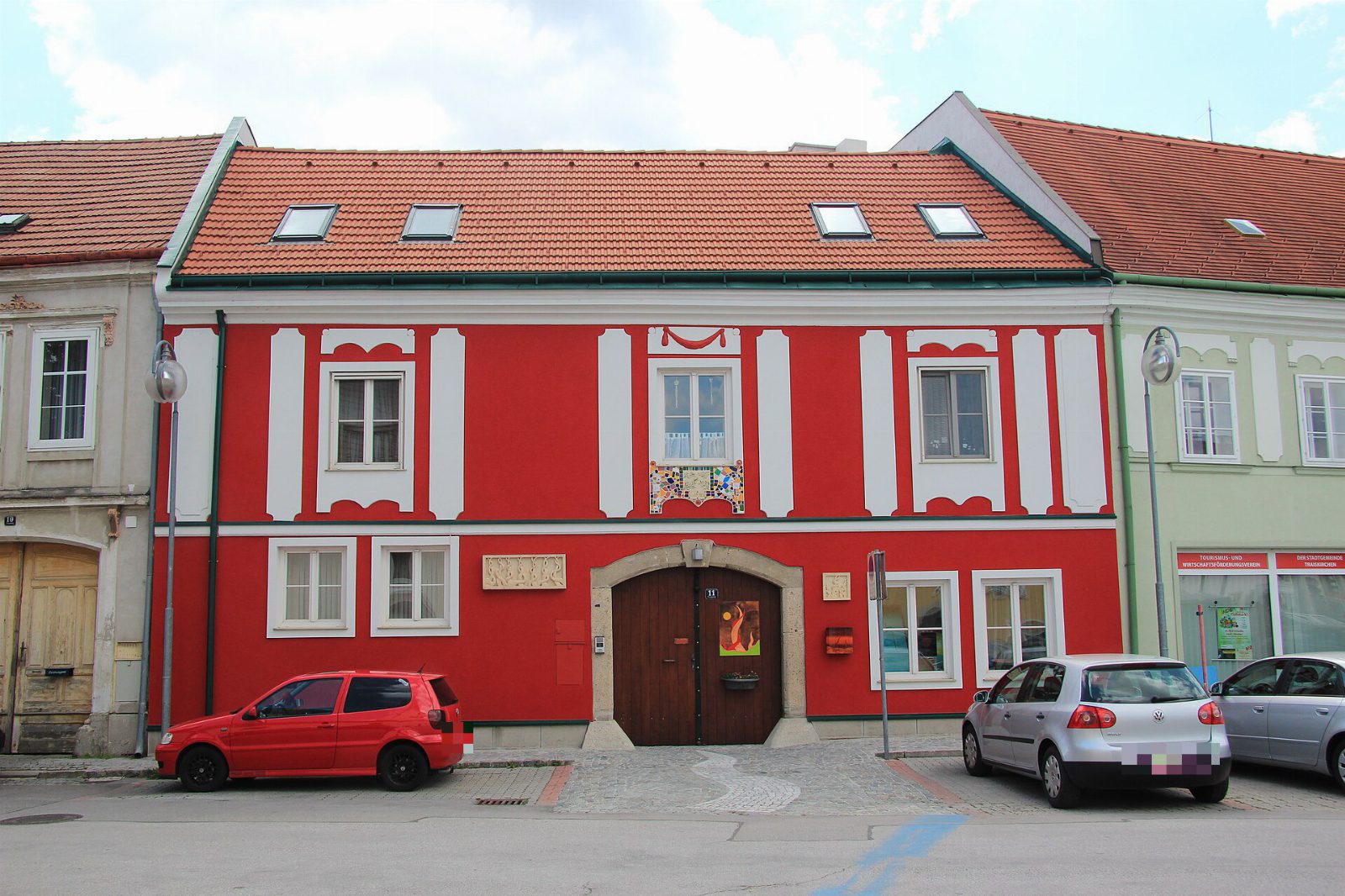Rotes Bürgerhaus mit weißen Fensterrahmungen und Holztor in Traiskirchen, davor parkende Autos