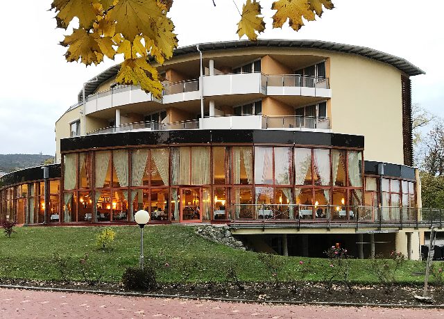 Rundbau des Vivea Gesundheitshotels in Bad Vöslau mit beleuchteter Glasfront, davor gelbes Herbstlaub