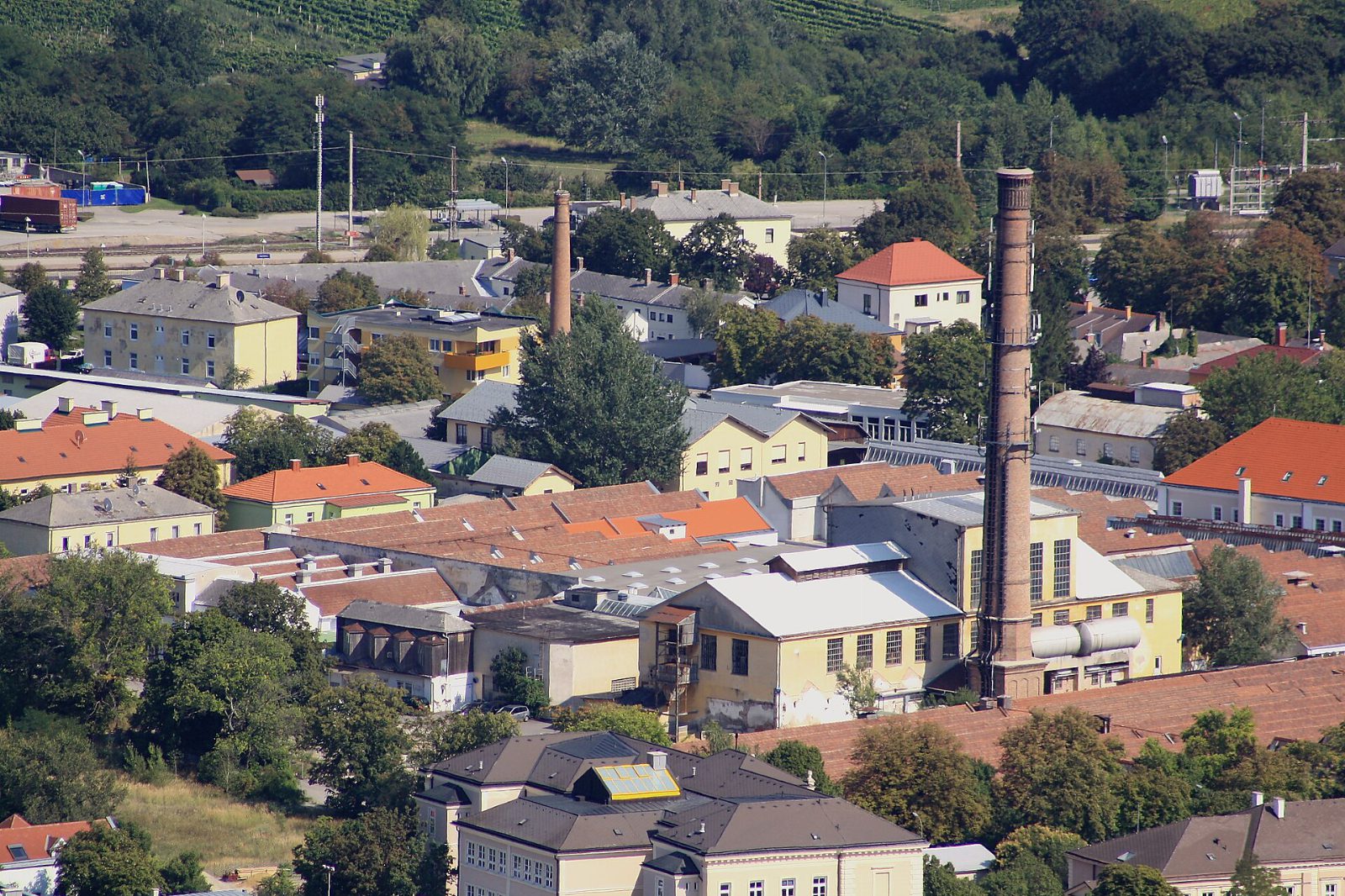 Blick von oben auf das Gelände der Vöslauer Kammgarnfabrik mit hohem Ziegelschlot und Hallendächern