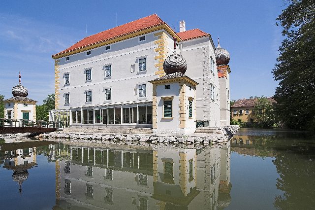 Wasserschloss Kottingbrunn mit weißer Fassade, rotem Dach und Zwiebeltürmchen, das sich im Schlossteich spiegelt