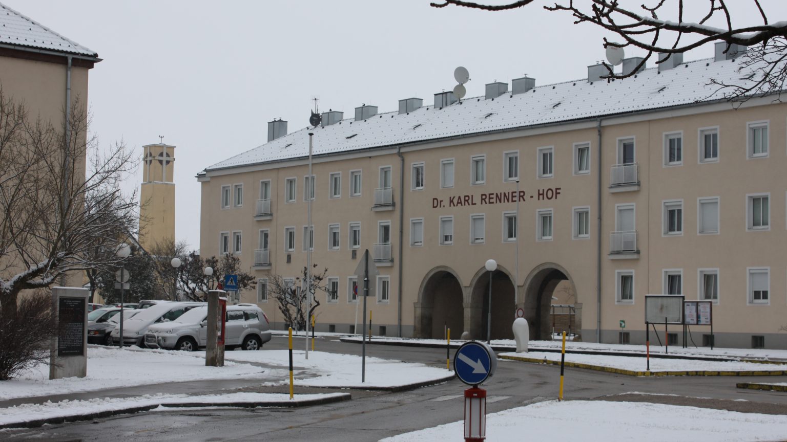 Der Dr.-Karl-Renner-Hof in Wiener Neustadt im Winter: langgestreckter Wohnbau mit drei Torbögen und dem Schriftzug Dr. Karl Renner-Hof