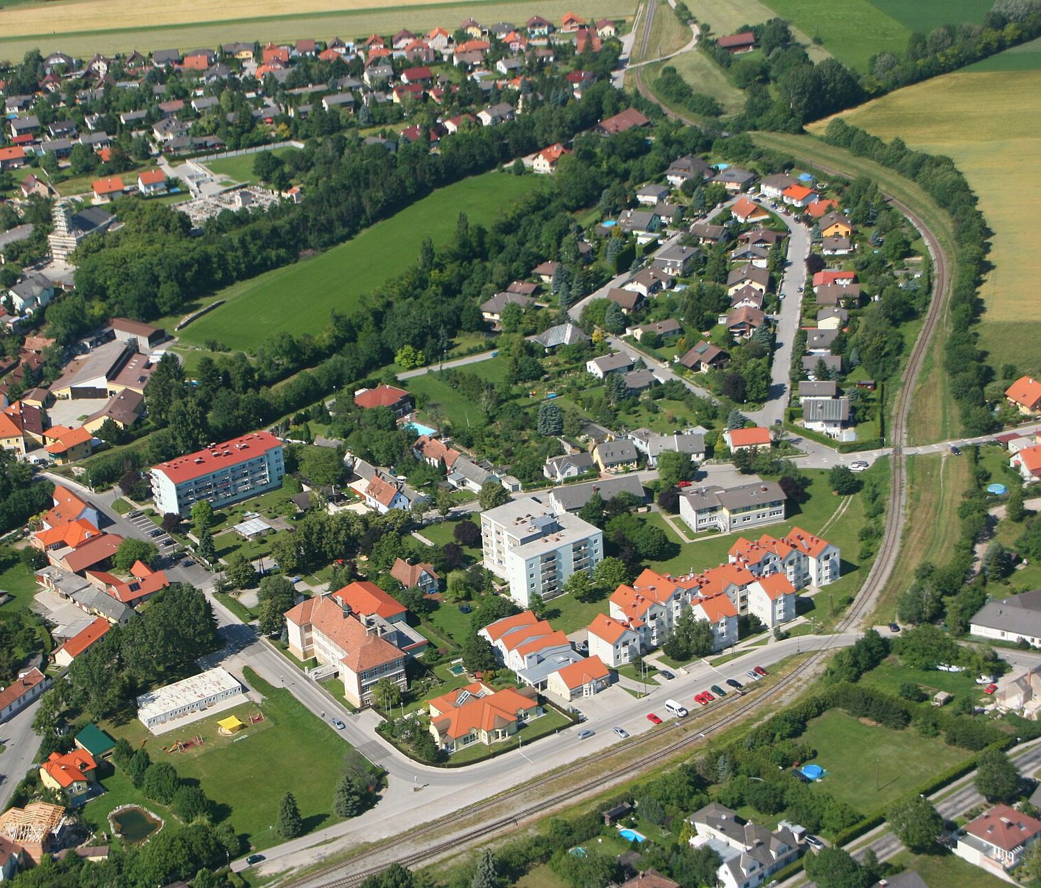 Luftbild von Wöllersdorf-Steinabrückl mit Wohnhäusern und Bahnstrecke. Ortsansicht, nicht die Tankstelle