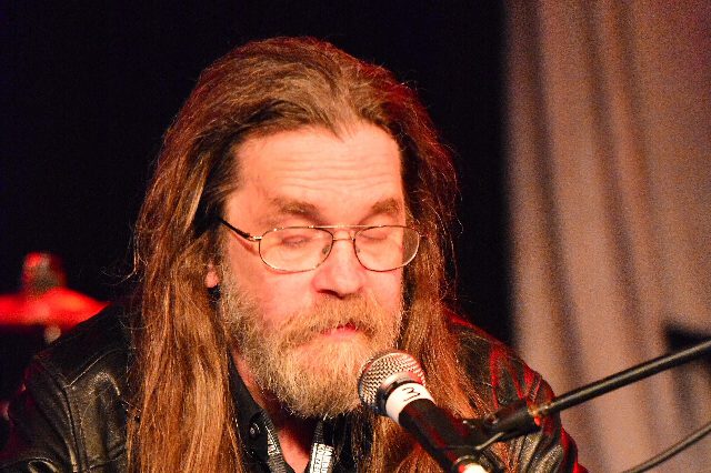 Wolfgang Hohlbein mit langen Haaren, Bart und Brille liest 2014 bei einer Lesung in Hamburg an einem Mikrofon