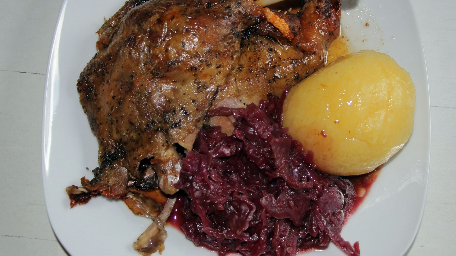 Symbolbild: Martinigansl mit Rotkraut und Erdäpfelknödel auf einem weißen Teller