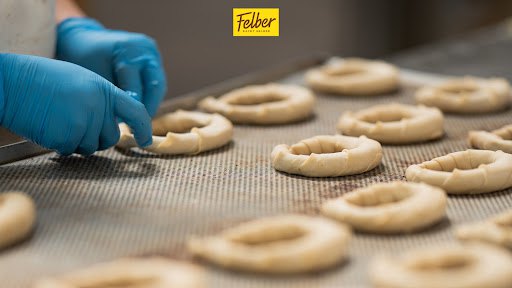 Blau behandschuhte Hände formen Gebäck auf einem Backblech; darüber das Felber-Logo.