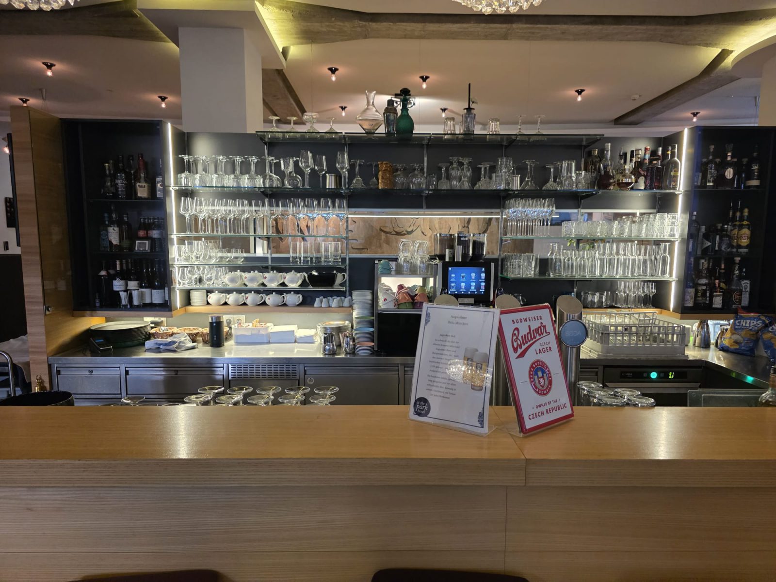 Bar im At the Park Hotel in Baden: heller Holztresen, dahinter beleuchtete Glasregale mit Gläsern und Flaschen