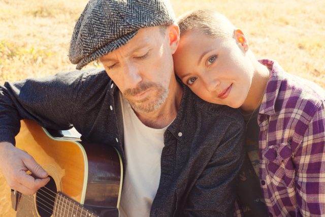 Genna & Jesse eng beieinander, er mit Kappe und Akustikgitarre, in warmem Gegenlicht