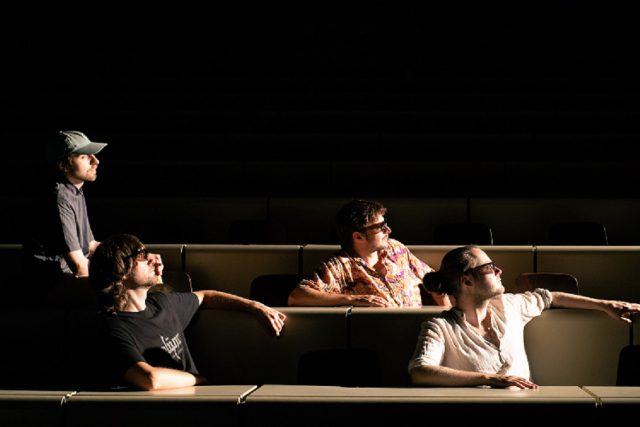 Die vier Musiker von MENÜ24 in Sitzreihen eines dunklen Saals